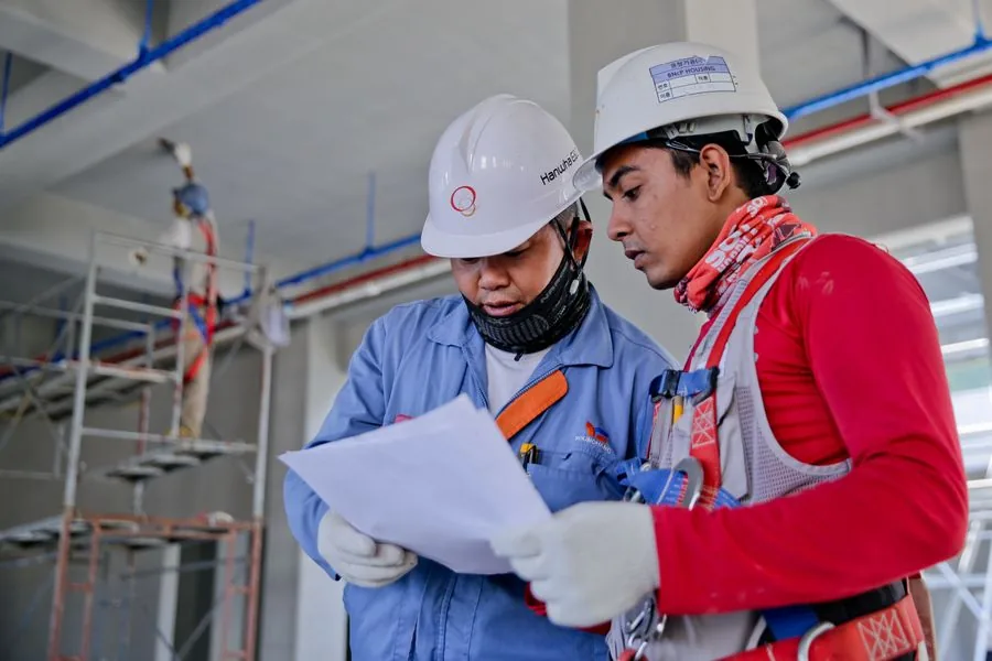 Two engineers in safety helmets reviewing construction plans on site
