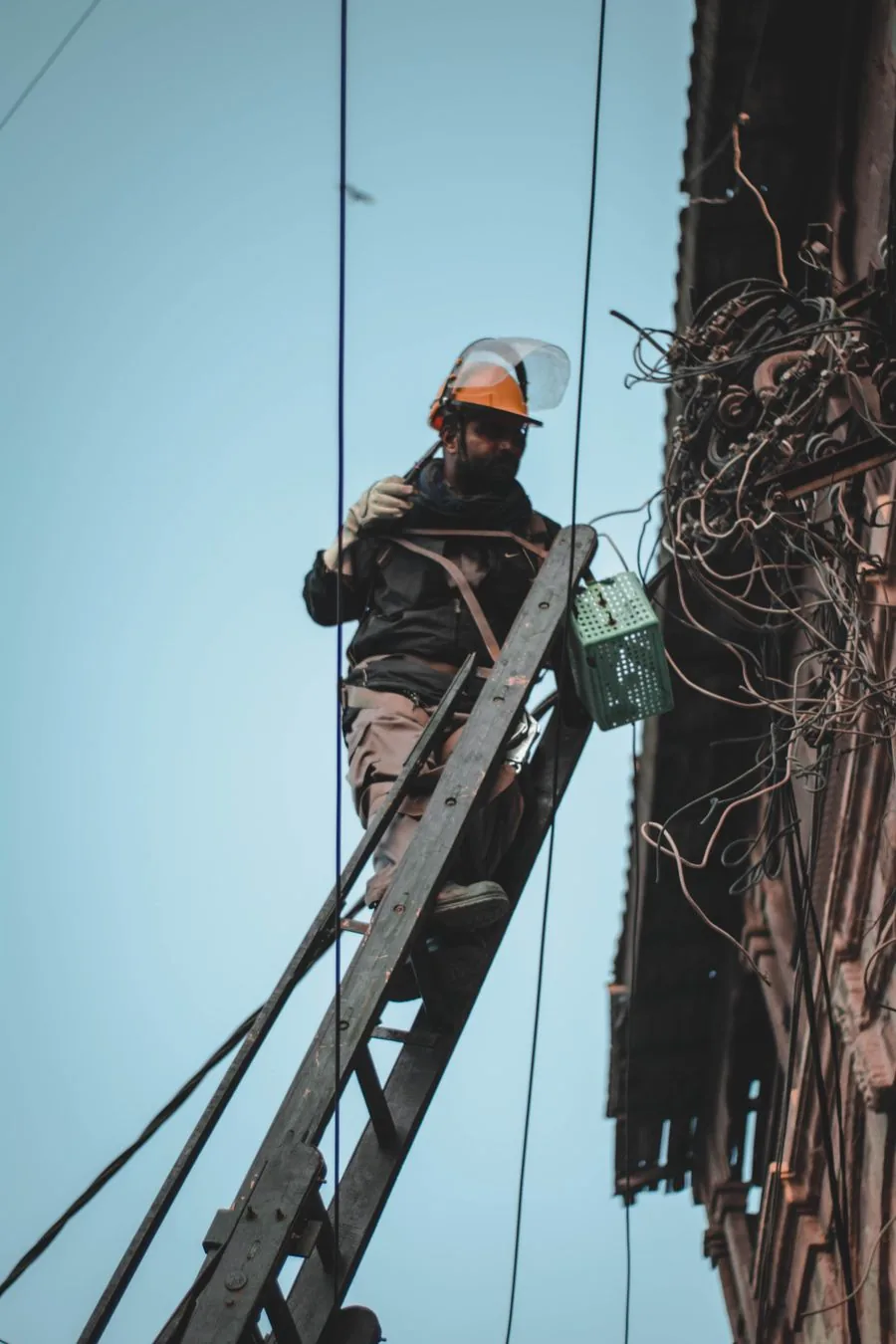 A worker repairing public power lines from a ladder