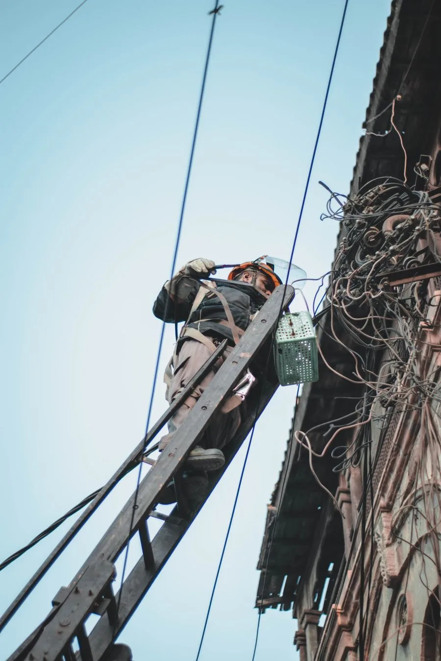 An electrician working on a building's power lines from a ladder