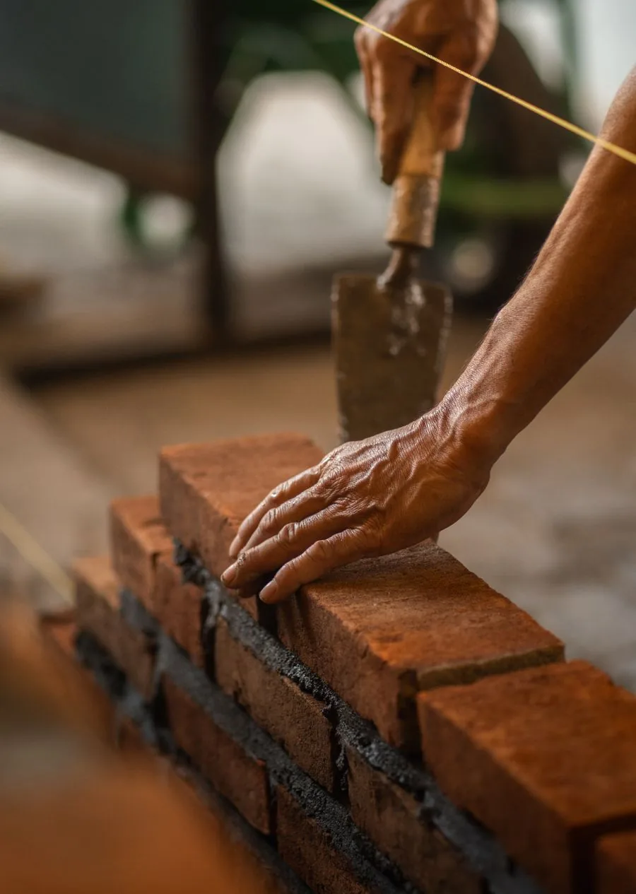 A mason's hands laying bricks with mortar
