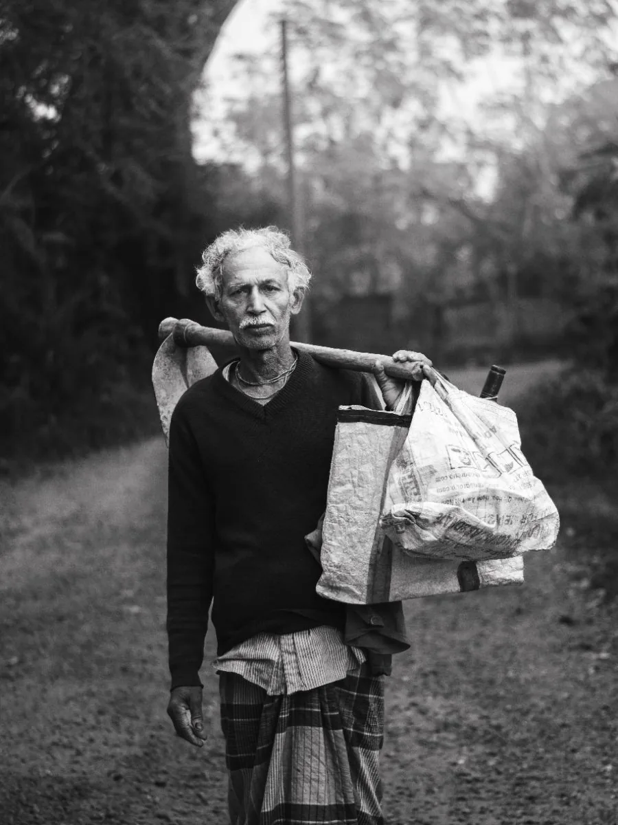 A worker with a spade over his shoulder and his bag, on a village road